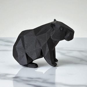 May include: A black, geometric capybara figurine. The sculpture is made of matte black material and features a faceted design, giving it a modern, angular appearance. The capybara is depicted in a seated position.