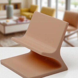 May include: A contemporary phone stand in a muted, earthy colour. The stand has a square base and a curved back, designed for a phone or tablet. It's made from a solid material with a smooth finish, suitable for a modern interior.