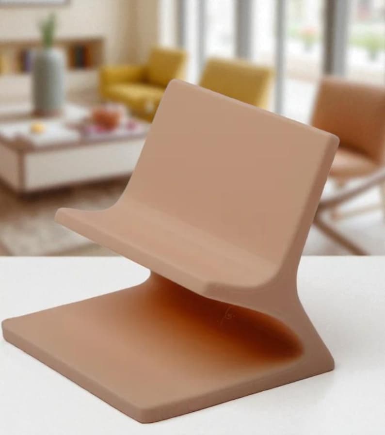 May include: A contemporary phone stand in a muted, earthy colour. The stand has a square base and a curved back, designed for a phone or tablet. It's made from a solid material with a smooth finish, suitable for a modern interior.