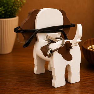 May include: A wooden dog-shaped eyeglasses and key holder. The holder is white with brown spots and ears. Black eyeglasses rest on the dog's head, and a set of keys hangs from the tail. The holder is on a wooden surface.