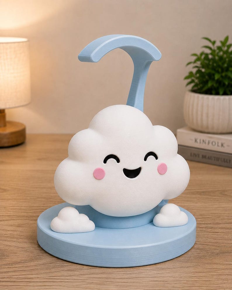 May include: A whimsical cloud-shaped night light in white and light blue. The cloud has a smiling face with pink cheeks and sits on a round base. A curved light arm extends from the base. The lamp is designed for a child's room.