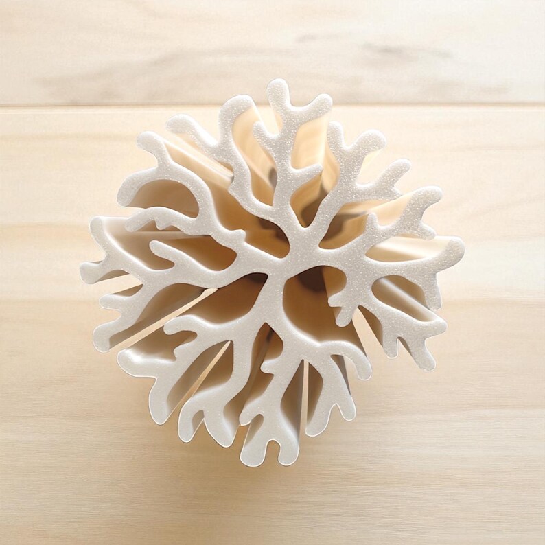 May include: A white, coral-shaped decorative object with intricate branching patterns. The object is made of a textured material and is set against a light wooden background. The design resembles a snowflake or a piece of coral.