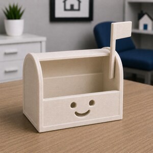 May include: A light beige mailbox-shaped desk organiser with a smiling face cutout. The mailbox has a flag on the side and a slot for mail. The organiser is made of a light-coloured material and sits on a wooden surface.