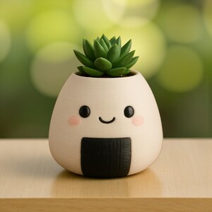 May include: A white, egg-shaped planter with a smiling face, pink cheeks, and a black seaweed-like design. The planter holds a green succulent plant. The planter is on a wooden surface.
