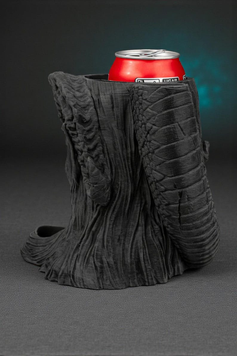 May include: A black, textured, 3D-printed can holder shaped like a tree trunk with a snake-like arm. A red can with white text is inside the holder. The holder is on a dark background.