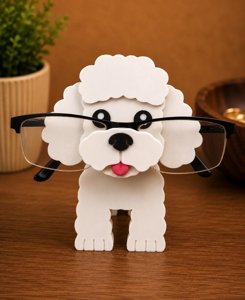 May include: A white poodle-shaped eyeglass holder with black rimmed glasses. The holder has a pink tongue and black eyes and nose. The eyeglass holder is made of a solid material and sits on a wooden surface.
