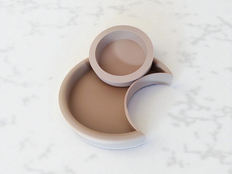Puede incluir: Un juego de bandejas decorativas modernas y minimalistas en tonos beige y topo. El conjunto incluye un cuenco circular sobre una bandeja en forma de media luna y una bandeja semicircular m&aacute;s grande.