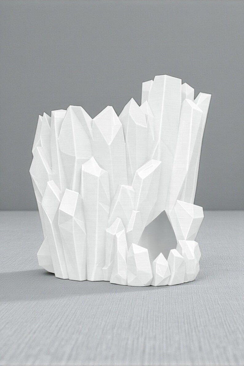 May include: A white, geometric crystal-shaped decorative object. The object has a hollow center and is composed of numerous angular, pointed shapes, resembling a cluster of crystals. The design is modern and minimalist, with a clean, monochromatic aesthetic.