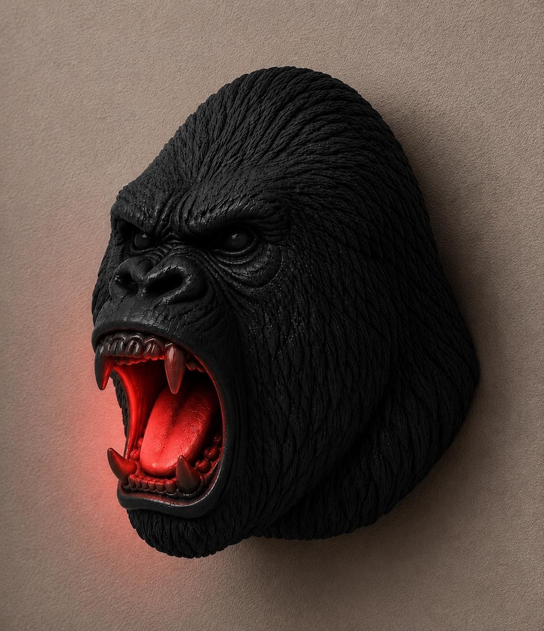 May include: A black gorilla head sculpture with an open mouth revealing red lighting. The sculpture has detailed fur texture and is mounted on a neutral-colored wall. The gorilla's teeth are visible.