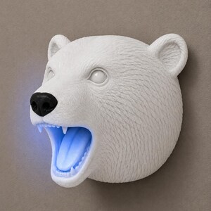 May include: A white polar bear head sculpture with a black nose and open mouth. The interior of the mouth glows with a blue light. The sculpture has detailed fur texture and is mounted on a neutral-toned wall.