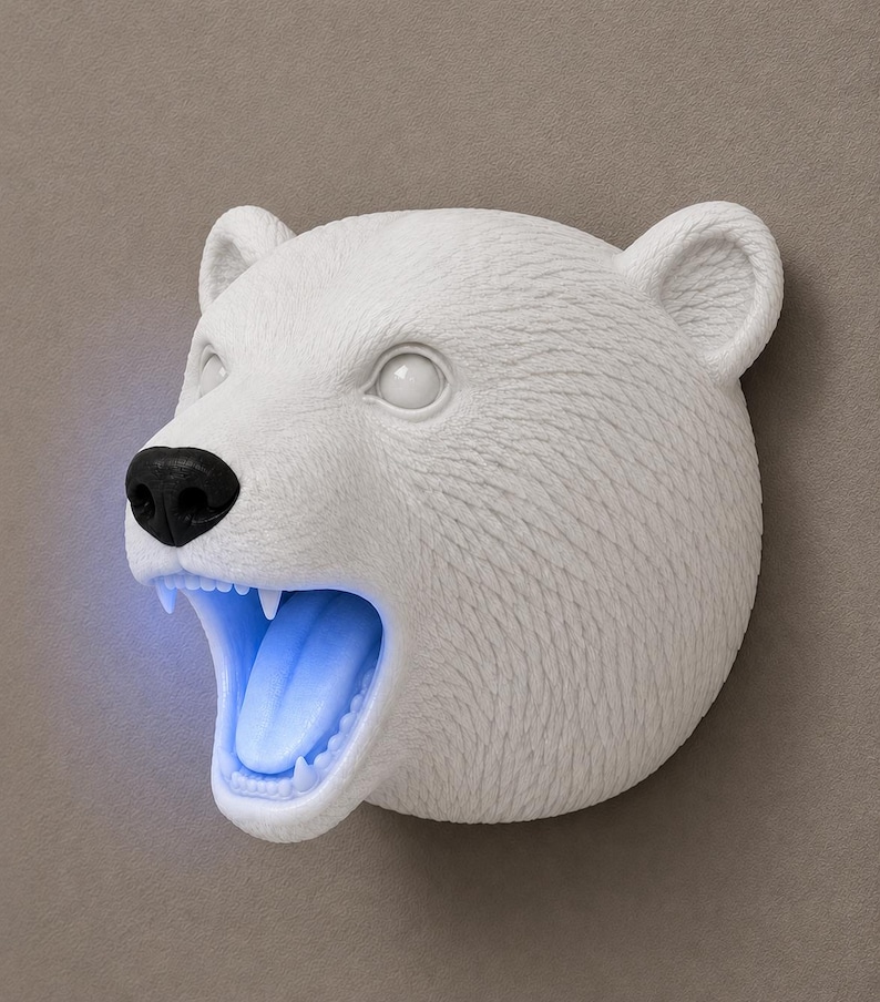 May include: A white polar bear head sculpture with a black nose and open mouth. The interior of the mouth glows with a blue light. The sculpture has detailed fur texture and is mounted on a neutral-toned wall.