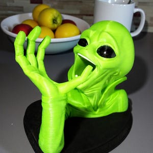May include: A neon green alien figurine with large black eyes and an open mouth, mounted on a black base. The alien's hand is raised, as if reaching out. The figurine is likely a decorative item or a unique piece of art.