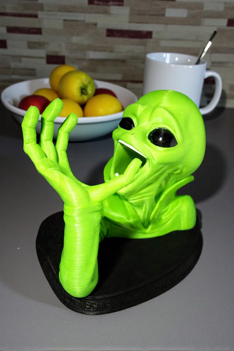 May include: A neon green alien figurine with large black eyes and an open mouth, mounted on a black base. The alien's hand is raised, as if reaching out. The figurine is likely a decorative item or a unique piece of art.
