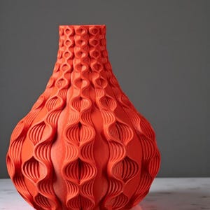 May include: A vibrant orange vase with a textured, repeating pattern. The vase has a bulbous body and a narrow neck. The surface design features a series of interconnected, elongated oval shapes, creating a visually interesting and modern aesthetic. The vase is a decorative home accent.