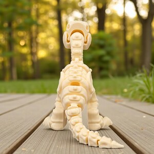 May include: A cream-colored dinosaur skeleton figurine, posed on a wooden deck. The toy dinosaur is facing away from the camera, showcasing its spine, tail, and leg structure. The background is a blurred view of a green lawn and trees.