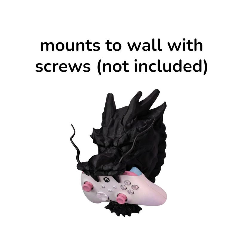 May include: A black dragon-shaped wall mount holding a white and pink Xbox controller. The controller has pink buttons and a blue accent. The text "mounts to wall with screws (not included)" is above the mount.