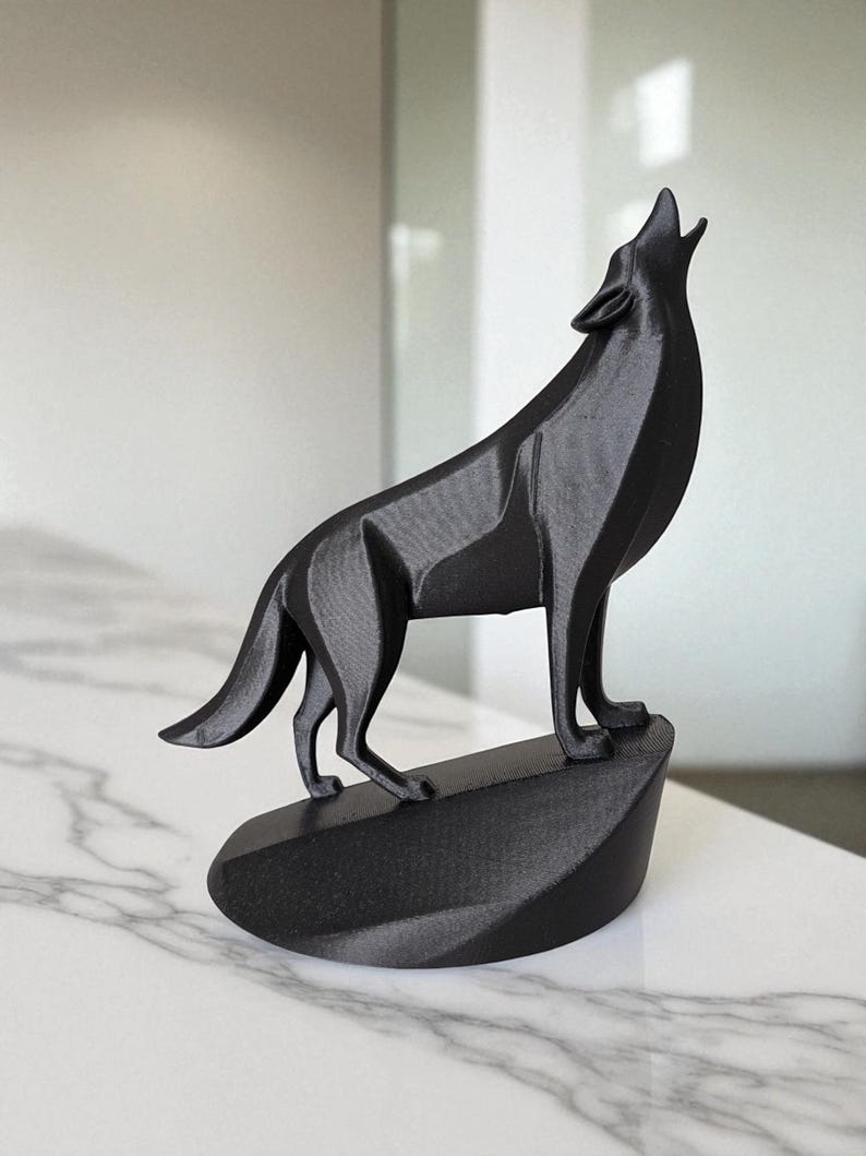 May include: A black 3D-printed sculpture of a howling wolf. The wolf is standing on a small, angled base. The sculpture has a geometric design and is displayed on a white marble surface.