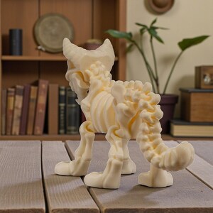 Puede incluir: Figura de esqueleto de gato de color crema, que muestra una estructura &oacute;sea detallada. La escultura est&aacute; sobre una superficie de madera, con una estanter&iacute;a y una planta en maceta en el fondo. El esqueleto del gato tiene cola y est&aacute; de pie.