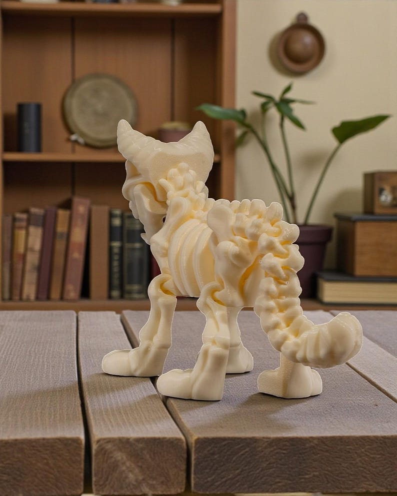 Puede incluir: Figura de esqueleto de gato de color crema, que muestra una estructura &oacute;sea detallada. La escultura est&aacute; sobre una superficie de madera, con una estanter&iacute;a y una planta en maceta en el fondo. El esqueleto del gato tiene cola y est&aacute; de pie.