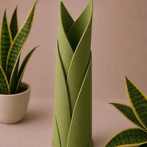 May include: A green, cylindrical vase with a leaf-like design. The vase is made of a textured material and has a round base. Two potted snake plants with yellow-edged green leaves are in the background.