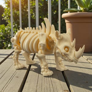 May include: A cream-colored rhinoceros skeleton figurine. The detailed model features a rib cage, spine, and skull with a prominent horn. The figurine is displayed on a wooden deck, showcasing its intricate design and skeletal structure.