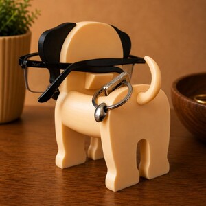 Pu&ograve; includere: Un portacavi a forma di cane, di colore beige chiaro, con dettagli neri sulle orecchie. Il supporto ha un portachiavi attaccato alla coda e tiene un paio di occhiali con montatura nera. Un oggetto decorativo per la casa o l'ufficio.