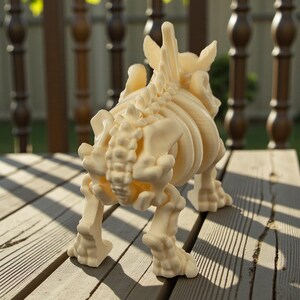 May include: A cream-colored, 3D-printed dinosaur skeleton figurine. The model is posed in a walking stance, showcasing the intricate details of the rib cage, spine, and leg bones. The figurine is displayed on a wooden surface.