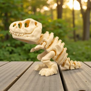 May include: A cream-colored, articulated dinosaur skeleton toy, likely a Tyrannosaurus Rex, is posed on a wooden surface. The toy features detailed bone structures, including a skull with visible teeth and eye sockets, and a segmented spine and tail.