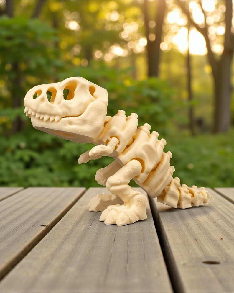 May include: A cream-colored, articulated dinosaur skeleton toy, likely a Tyrannosaurus Rex, is posed on a wooden surface. The toy features detailed bone structures, including a skull with visible teeth and eye sockets, and a segmented spine and tail.