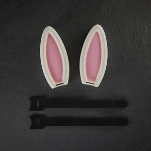 May include: Two white bunny ears with pink interiors and two black adjustable straps.