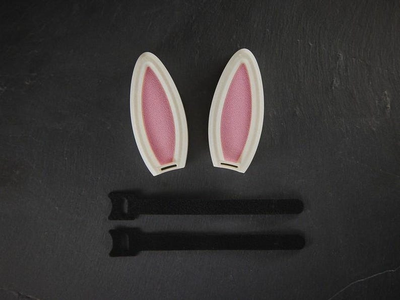 May include: Two white bunny ears with pink interiors and two black adjustable straps.
