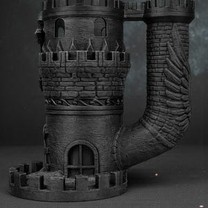 May include: A black, 3D-printed castle-shaped mug. The mug features two towers connected by a bridge, with detailed brickwork, arched windows, and crenelated battlements. The handle is a curved tower with a wing design.