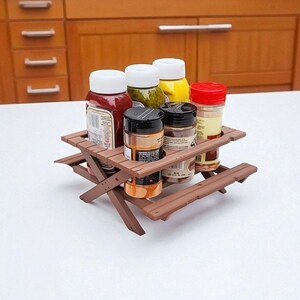 Puede incluir: Una mesa de picnic marr&oacute;n en miniatura contiene varias botellas de condimentos con tapas blancas, rojas y amarillas. Los condimentos incluyen ketchup, mostaza y especias. La mesa es de madera y tiene un dise&ntilde;o cl&aacute;sico de mesa de picnic.