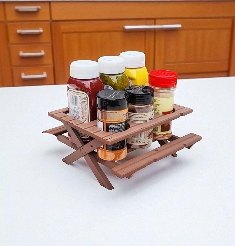 Puede incluir: Una mesa de picnic marr&oacute;n en miniatura contiene varias botellas de condimentos con tapas blancas, rojas y amarillas. Los condimentos incluyen ketchup, mostaza y especias. La mesa es de madera y tiene un dise&ntilde;o cl&aacute;sico de mesa de picnic.