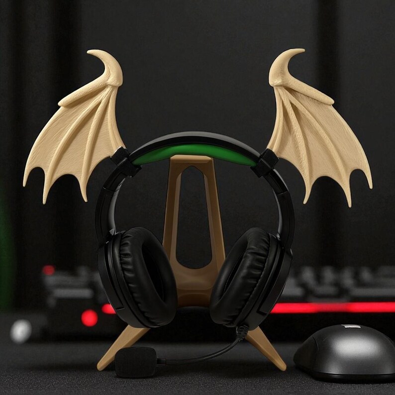 May include: A black gaming headset with a green accent sits on a beige stand, with beige bat wings on either side. A black mouse is to the right. The headset has a microphone and is designed for gaming.