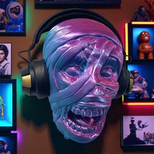 May include: A wall-mounted sculpture of a mummy's head, painted in shades of blue and purple, wearing black headphones with gold accents. The mummy's mouth is open, revealing teeth. The background includes framed artwork and figurines.