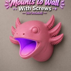 May include: A pink axolotl-shaped wall mount with an open mouth and a purple glow inside. The text "Mounts to Wall With Screws (Not Included)" is above the axolotl. The axolotl has detailed gills and a smooth finish.