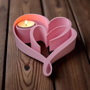 May include: A pink heart-shaped candle holder with a lit tea light candle. The holder has a layered design with a decorative heart shape. The candle holder is made of a solid material and sits on a wooden surface.