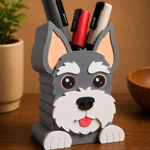 May include: A gray and white dog-shaped desk organizer holding pens. The organizer has a cartoon-like design with a black nose, big eyes, and a red tongue. The organizer is holding black, red, and white pens.