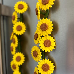 May include: A decorative sunflower garland with bright yellow petals and brown centers. The sunflowers are attached to green stems, creating a vibrant and cheerful floral arrangement. Perfect for adding a touch of summer to any space.
