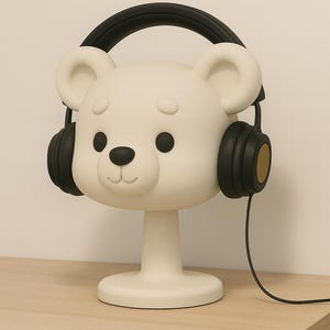 May include: A whimsical white bear-shaped lamp with black headphones. The lamp has a round base and a stem, and the bear's face features black eyes and a nose. The headphones are black with gold accents. The lamp is on a wooden surface.