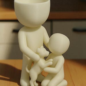 May include: A cream-colored figurine depicts a family scene. A tall figure with a bowl-shaped head holds a small dog, while a smaller figure kneels, also interacting with the dog. The figures are on a wooden surface.