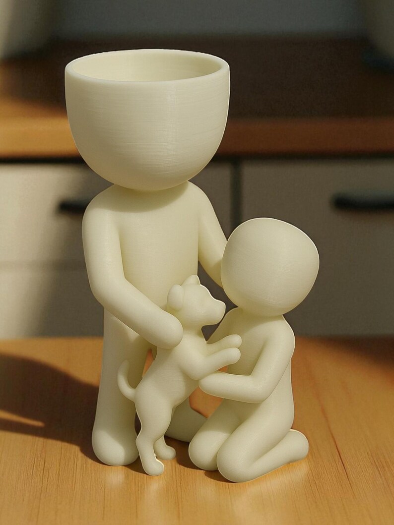 May include: A cream-colored figurine depicts a family scene. A tall figure with a bowl-shaped head holds a small dog, while a smaller figure kneels, also interacting with the dog. The figures are on a wooden surface.