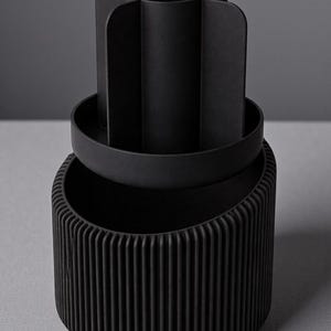 May include: A black desk organizer with a ribbed base, a circular tray, and a top section divided into four compartments. The organizer is made of a matte material and sits on a gray surface.