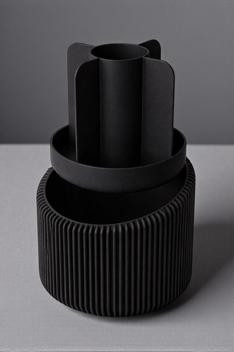 May include: A black desk organizer with a ribbed base, a circular tray, and a top section divided into four compartments. The organizer is made of a matte material and sits on a gray surface.