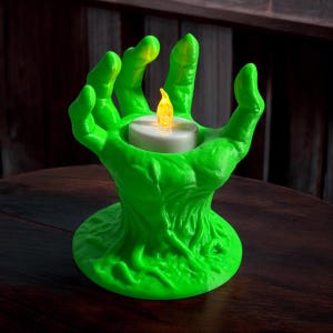 May include: A neon green hand-shaped candle holder with a battery-operated candle. The candle holder has a textured surface and a round base. The candle has a white exterior and a flickering yellow light.