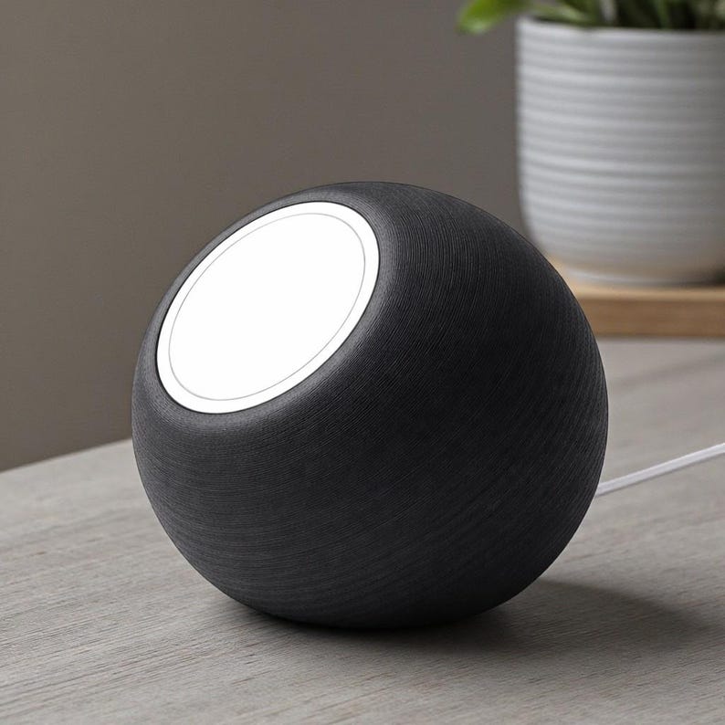 May include: A black, spherical wireless charger with a white charging surface. The charger has a textured, wood-like appearance and a white cable. The design is modern and minimalist, suitable for a desk or bedside table.