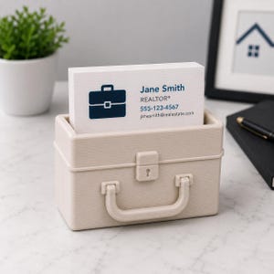May include: A beige business card holder in the shape of a small briefcase, filled with white business cards. The cards display a dark blue briefcase icon and the name "Jane Smith, REALTOR&reg;" with contact details.