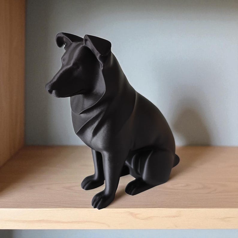 May include: A matte black dog sculpture in a seated position. The dog has a smooth, geometric design with pointed ears and a short tail. The sculpture is displayed on a light-colored wooden shelf against a pale blue wall.