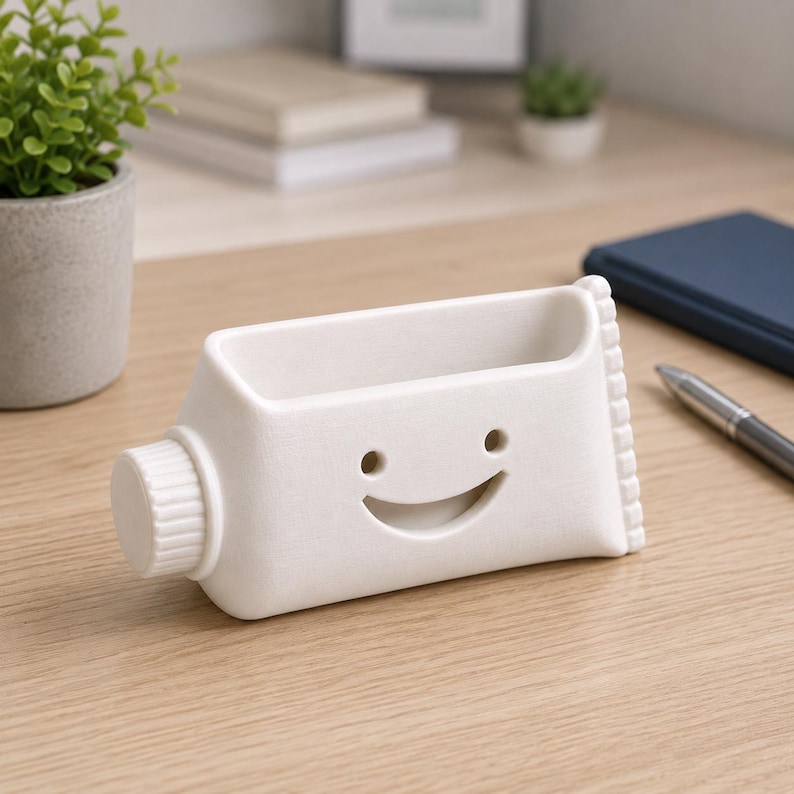 Pu&ograve; includere: Un organizer da scrivania in ceramica bianca a forma di tubetto di dentifricio, con un volto sorridente. L'organizer ha un vano rettangolare e un tappo a vite. Adatto per contenere penne, matite o piccoli accessori per l'ufficio.